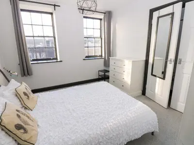 a white bedroom with a bed and two windows at Lowther Penthouse in Whitehaven