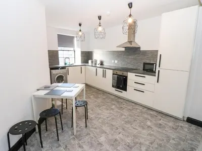 a kitchen with white cabinets and a table and stools at Lowther Penthouse in Whitehaven