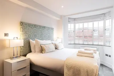 a white bedroom with a large bed and a window at Stylish Chelsea Flat Near Sloane Square in Moffat