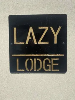 a black sign with the word laxy lodge on a wall at Lazy Lodge in Foxdale