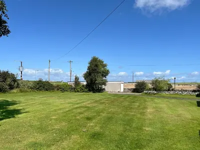a large grass field with a tree in the middle at 3 Laigh Isles in Kirkcudbright