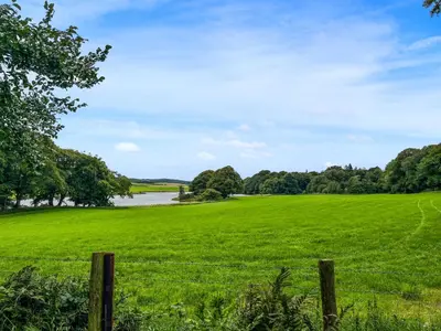 a field of green grass with a fence and a river at Andromeda - Uk50359 in Castle Douglas