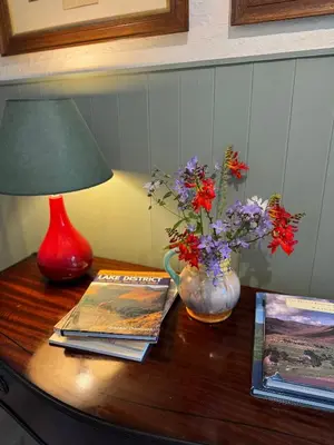 a table with a lamp and books and flowers on it at 1 Laithes Cottages in Skelton