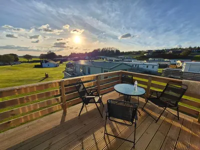 a patio with a table and chairs on a deck at Three Lochs Holiday Park- Lochwood Caravan in Newton Stewart