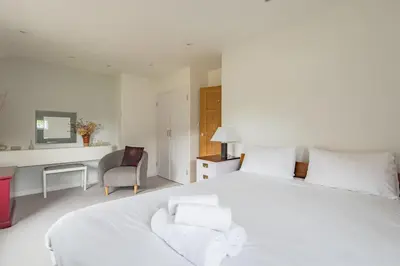 a white bedroom with a large white bed and a chair at St Mary's House by Keepers Cottages in Moffat