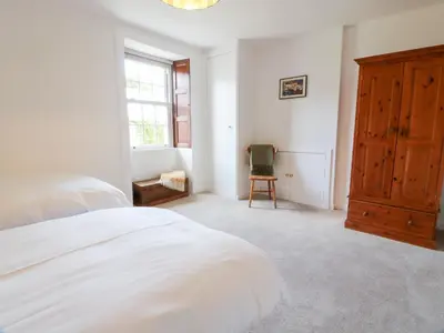 a white bedroom with a bed and a wooden cabinet at Balsaggart Farm in Maybole