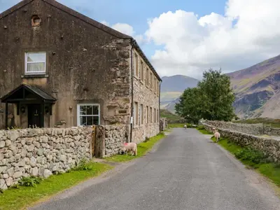 an old stone building with sheep standing next to a road at Buckbarrow in Seascale