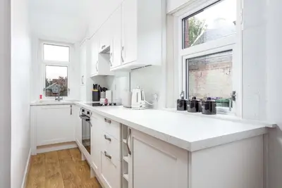 a white kitchen with white cabinets and a window at The Bay Suite - Donnini Apartments in Troon