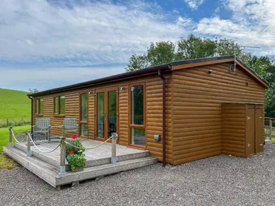 a wooden cabin with a porch and a deck at Alderneuk Lodge - Uk49923 in Dumfries