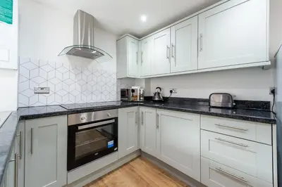 a kitchen with white cabinets and black counter tops at 5 Bed Workington House with Parking Near Station in Workington
