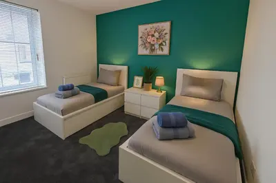 a bedroom with two beds and a green wall at Armstrong St - Cosy 3 Bedroom Home in Workington