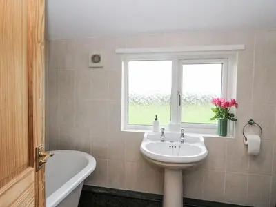 a bathroom with a sink and a tub and a window at Daisy Cottage in Wigton