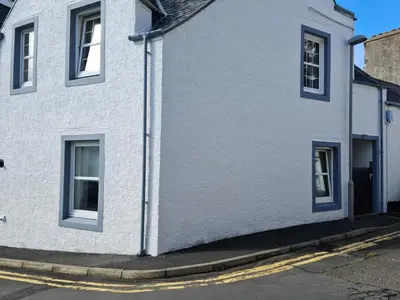 a white house with blue windows on a street at The Attic Portpatrick in Portpatrick