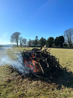 a pile of fire in a field next to a body of water at Stylish Cabin with Countryside Views and King Bed in Maybole