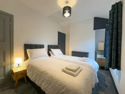 a bedroom with two beds with white sheets and a lamp at Coastal Lakes Mews Cottage