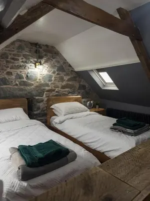 two beds in a room with a stone wall at Pink Cottage in Kirkcowan