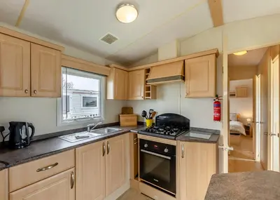 a kitchen with wooden cabinets and a stove top oven at Rowanbank Caravan Park in Beckfoot