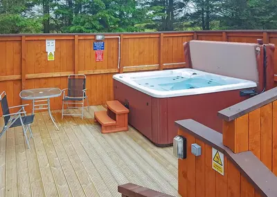 a hot tub on a deck with a table and chairs at Whitecairn Holiday Park in Glenluce