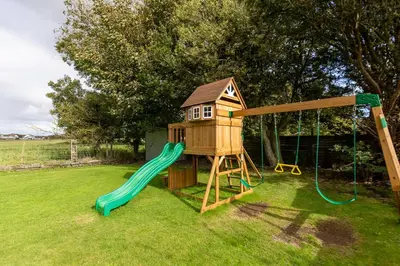 a playground with a house and a slide at EASTCOTE FARM - Spacious 5-Bed Home with Views, Garden & Playroom in Silloth