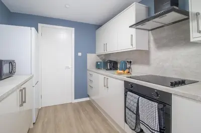 a kitchen with white cabinets and blue walls at Corsehill Cottage - 3 Bedroom, 2 bathroom House in Dreghorn
