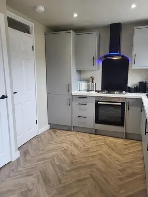 a kitchen with white cabinets and a wooden floor at The MacIntyre - Coorie Doon Stays in Kilmarnock