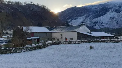 a house in the snow with mountains in the background at Hot tub, Mountain View, 4-poster bed and log burner in Borrowdale Valley