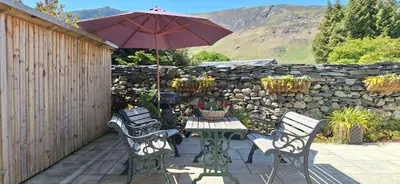 a patio with a table and chairs and an umbrella at 2 Double Bed Cottage Hottub Lake District Keswick in Keswick
