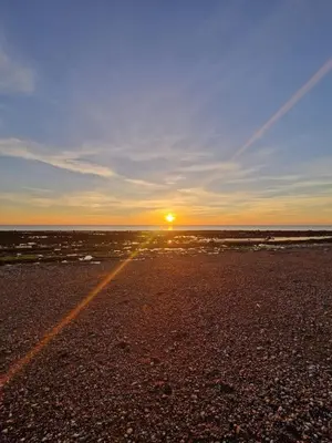 a sunset on a beach with the sun in the distance at Seaside Retreat in Harrington