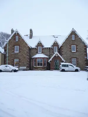 a large brick building with two cars parked in a parking lot at The Hopetoun Arms Hotel in Leadhills