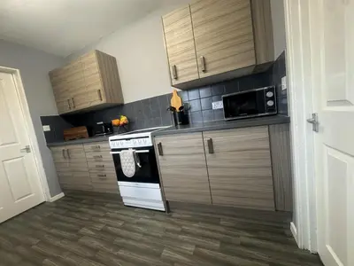 a kitchen with wooden cabinets and a stove and microwave at West Lakes 3 Bedroom - Sleeps 5 - Self Check In - Fully Furnished House in Workington