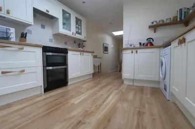a large kitchen with white cabinets and wooden floors at Moir Cottage in Portpatrick