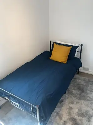 a bed with a blue comforter and a yellow pillow at London Cozy Single Room in Moffat