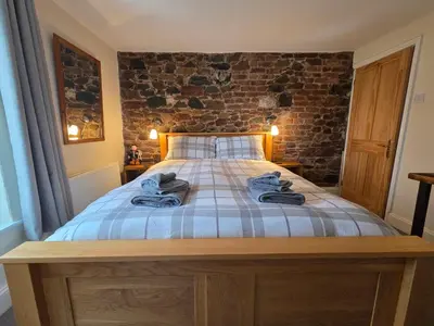 a bedroom with a bed with a brick wall at Feather Bed Cottage - Dog Friendly Lakeland Retreat with Log Burner & Garden