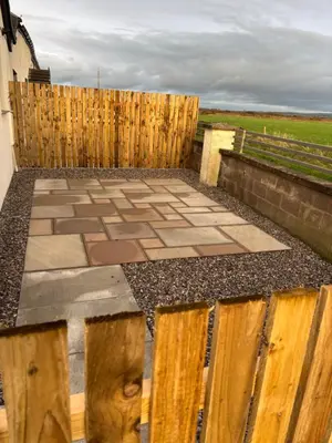 a patio with a wooden fence and a stone patio at Cross Beck Cottage in Allonby
