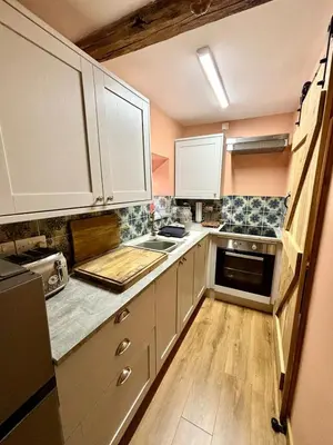 a kitchen with white cabinets and a wooden floor at Maggies Cottage in Little Broughton