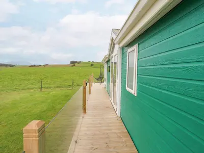 a blue building with a wooden walkway next to a field at No 8 Hillcote Lodge in Cockermouth