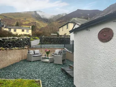 a patio with two chairs and a clock on a building at Garth Cottage in Keswick