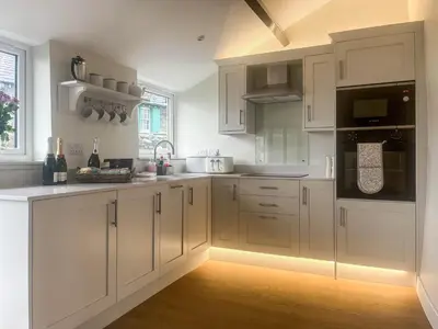 a white kitchen with white cabinets and black appliances at Garth Cottage in Keswick