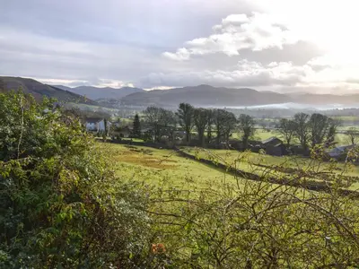 a green field with trees and mountains in the background at Derwent View in Applethwaite