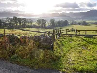 a fence on a grassy field with mountains in the background at Derwent View in Applethwaite
