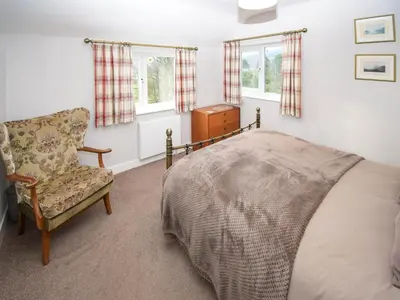 a bedroom with a bed and a chair and windows at Derwent View in Applethwaite