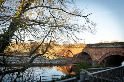 a brick bridge over a river with a tree at River View Cottages in Annan
