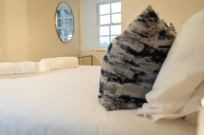 a pillow sitting on a white bed with a window at River View Cottages in Annan