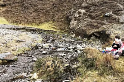 a couple of people sitting next to a river at 3 Millbeck Cottage in Keswick