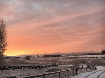a sunset in a field with snow and a fence at Barnharrow Holiday Park in Newton Stewart