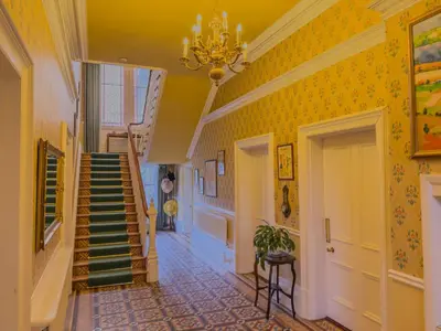 a hallway with yellow walls and stairs with a chandelier at Eden Mount, Wetheral, characteful, spacious home overlooking village green, close to M6 in Wetheral