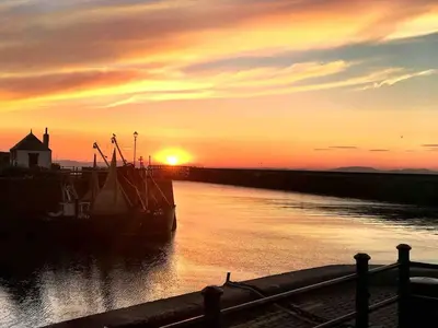 a boat sitting in the water at sunset at Cosy Cottage on edge of Lake District in Little Broughton