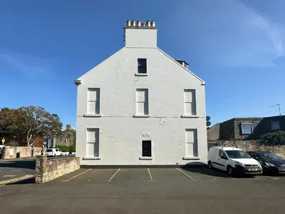 a white house with a car parked in a parking lot at The Penthouse - Beachwalk Apartments in Ayr