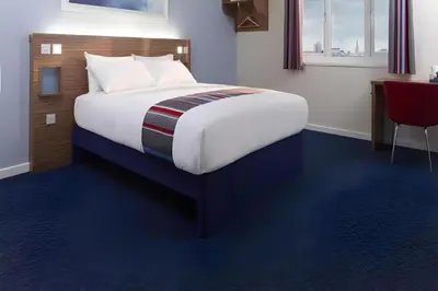 a large bed in a room with a red chair at Travelodge Dumfries in Collin