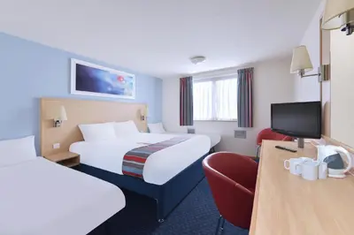 a hotel room with two beds and a chair at Travelodge Carlisle Todhills in Rockcliffe